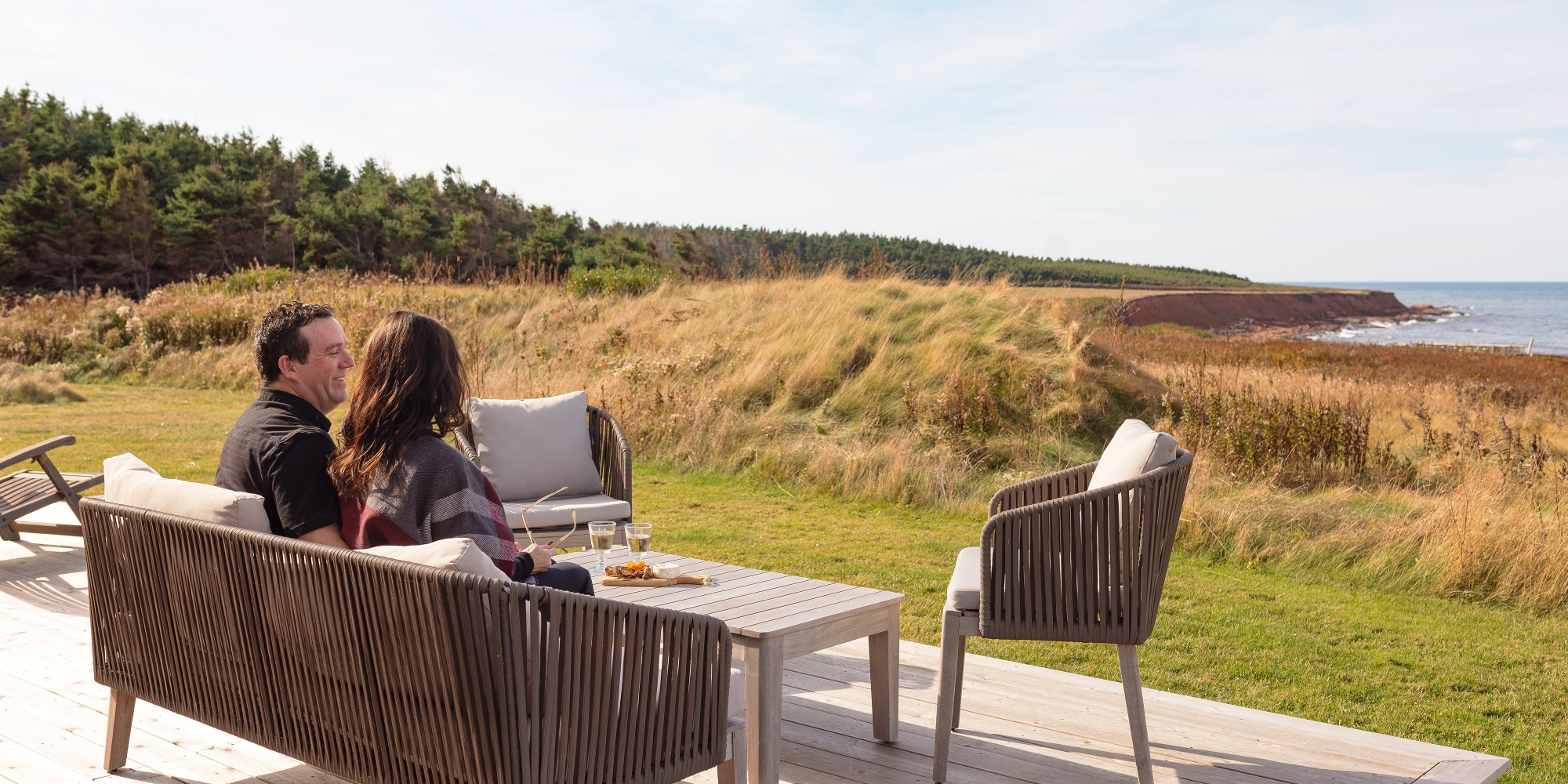 Couple sit on deck overlooking coastal view of red cliffs and water